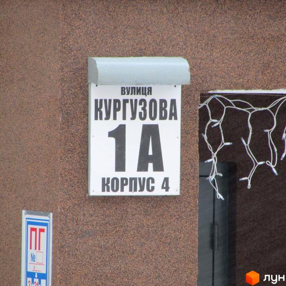 Табличка з назвою вулиці Кургузова, номер будинку 1А, корпус 4. На фото видно частину фасаду будівлі.