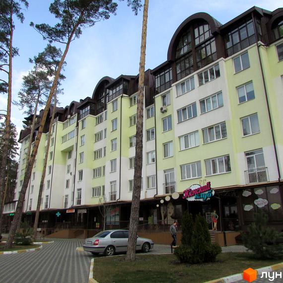 Зовнішній вигляд багатоповерхового житлового комплексу ЖК Ірпінські Липки з зеленими та білими фасадами та арочними дахами. На прибудинковій території розташовані дерева та доріжки.