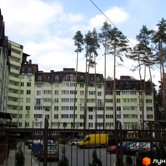 Зовнішній вигляд житлового комплексу ЖК Ірпінські Липки з зеленими фасадами та темними дахами. На прибудинковій території видно дерева та припарковані автомобілі.