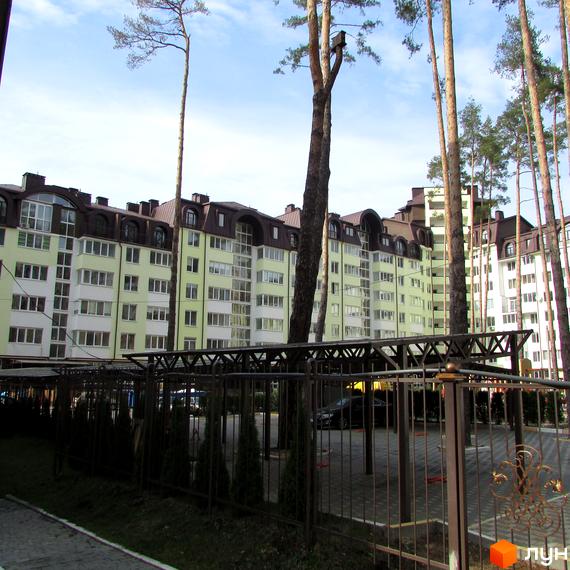 Житловий комплекс Ірпінські Липки. Багатоквартирні будинки світло-зеленого кольору з коричневими дахами, паркінг під навісом, зелені насадження та огорожа.