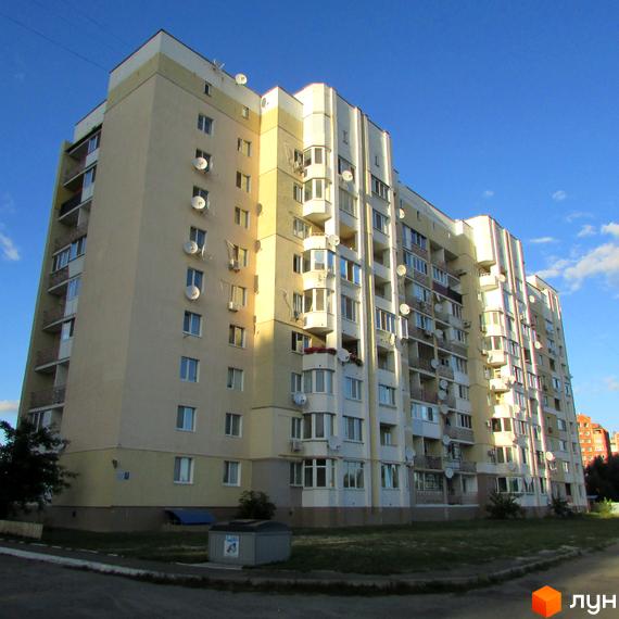 Житловий комплекс Уюткіно - багатоповерховий будинок з балконами та кондиціонерами. Навколо будинку зелена зона та доріжка.