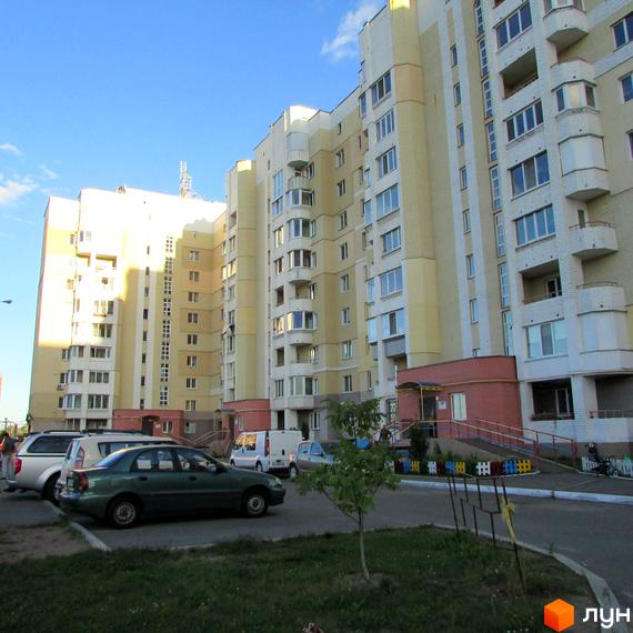 Житловий комплекс Уюткіно. Зовнішній вигляд багатоповерхових будинків з жовтою та білою обробкою фасаду. Прибудинкова територія з автомобілями та зеленими насадженнями.