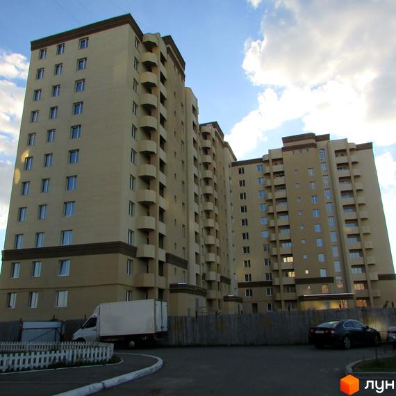 Вид на житловий комплекс Уюткіно з високими будинками та балконами. На прибудинковій території видно паркування з автомобілями та паркан.
