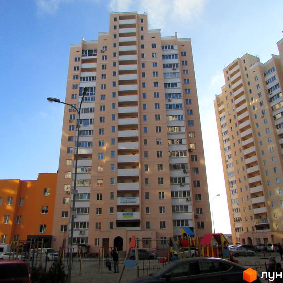 Житловий комплекс на вул. Грушевського, 21а. Багатоповерхові будинки світло-бежевого кольору з білими балконами. Поруч дитячий майданчик та парковка.