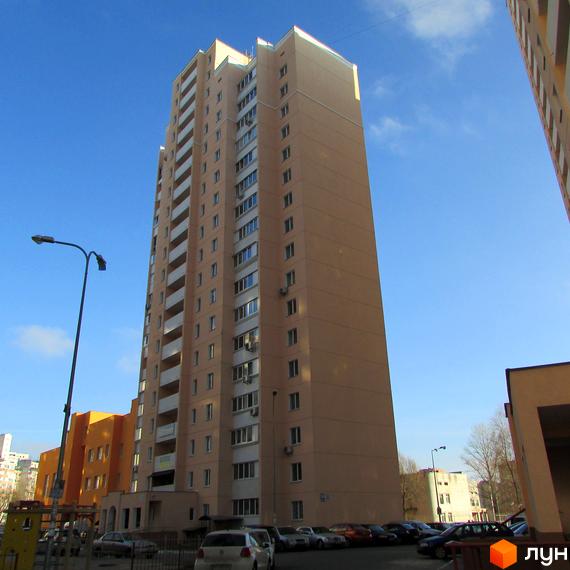 Високоповерховий житловий комплекс по вулиці Грушевського, 21а. Навколо будинку розташовані припарковані автомобілі та зелені насадження.