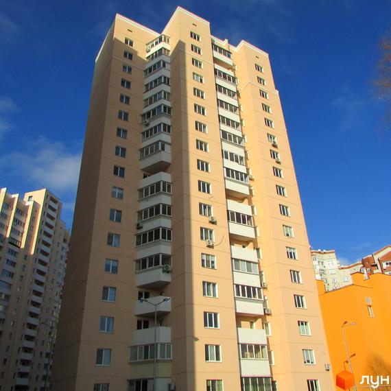 Високий світло-бежевий будинок з численними балконами та вікнами на фоні блакитного неба. Сусідній будинок також має світлий фасад та схожу архітектуру.