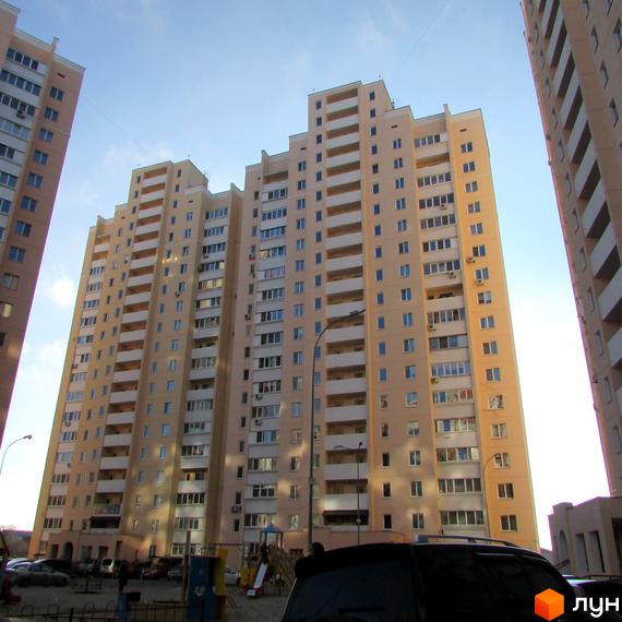 Зовнішній вигляд багатоповерхового житлового комплексу на вул. Грушевського, 21а. Навколо будинку розташована прибудинкова територія з дитячим майданчиком та автомобілями.