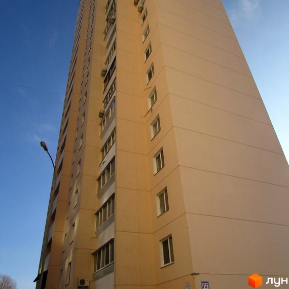 Зовнішній вигляд багатоповерхового будинку на вул. Грушевського, 21а. Фасад будівлі світло-бежевого кольору з численними вікнами та балконами. Навколо будинку блакитне небо.