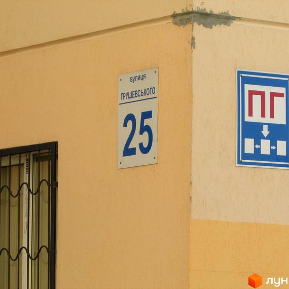 Фасад будинку №25 по вулиці Грушевського. На стіні видно табличку з назвою вулиці та номером будинку. Поруч розташована синя табличка з піктограмами.