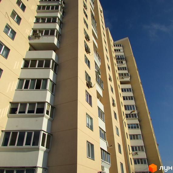 Фасад житлового комплексу на вул. Грушевського, 21а. Будинок має багатоповерхову структуру з балконами та вікнами, розташований на фоні блакитного неба.