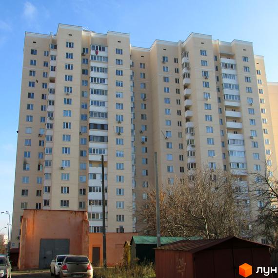 Багатоповерховий житловий комплекс на вулиці Грушевського, 21а. Будинок світло-бежевого кольору з численними вікнами та балконами. На передньому плані видно прибудинкову територію з гаражами та деревами.