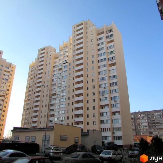 Високоповерховий житловий комплекс на вул. Грушевського, 21а. Багатоповерхові будинки світло-бежевого кольору з численними балконами та кондиціонерами. Навколо будівель розташовані припарковані автомобілі та зелені насадження.