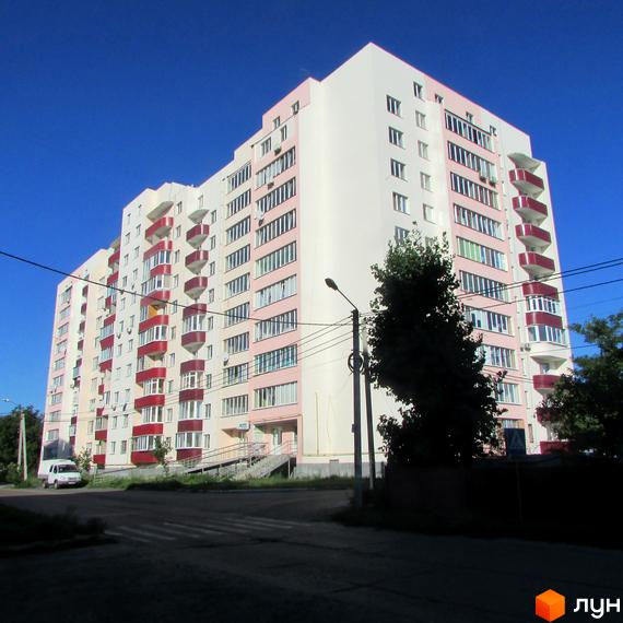 Житловий комплекс Лелека-1 – багатоповерховий будинок з рожевими та білими фасадами, балконами та кондиціонерами. Навколо будинку зелені насадження та дорога з пішохідним переходом.