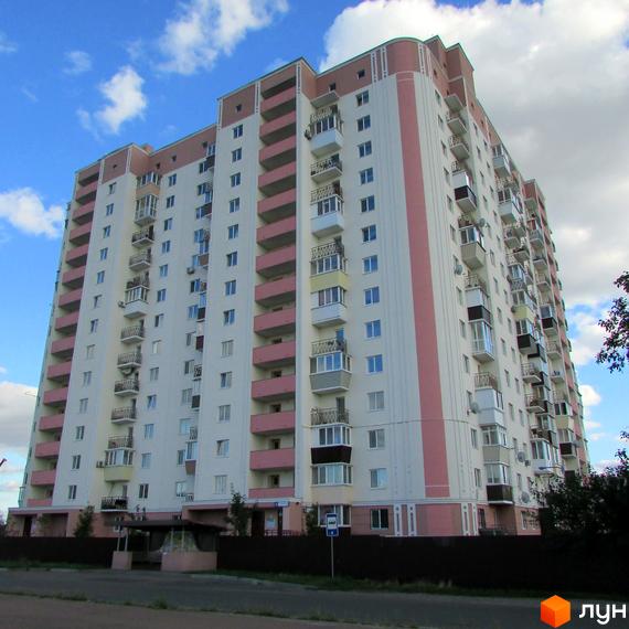 Багатоповерховий житловий комплекс Щасливі метри з рожевими та білими фасадами, балконами та вікнами. Навколо будинку видно зелені насадження та дорогу.