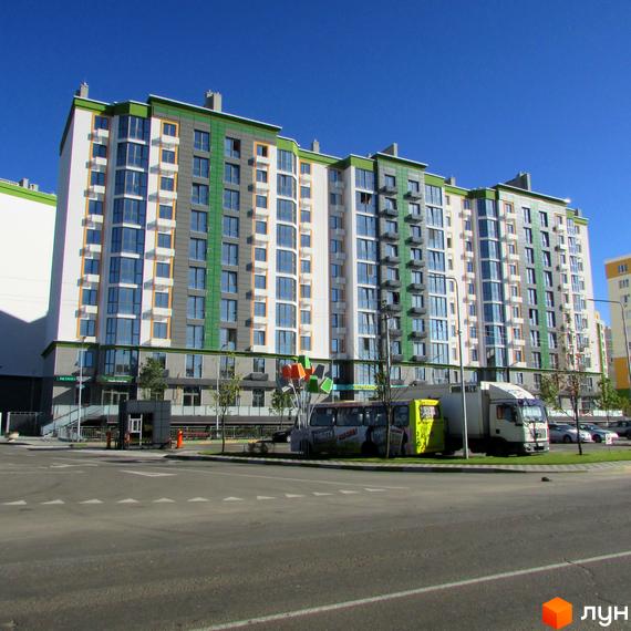 Зовнішній вигляд багатоповерхового житлового комплексу Евромісто з фасадом біло-зелено-сірого кольору. На прибудинковій території видно автомобілі та дерева.
