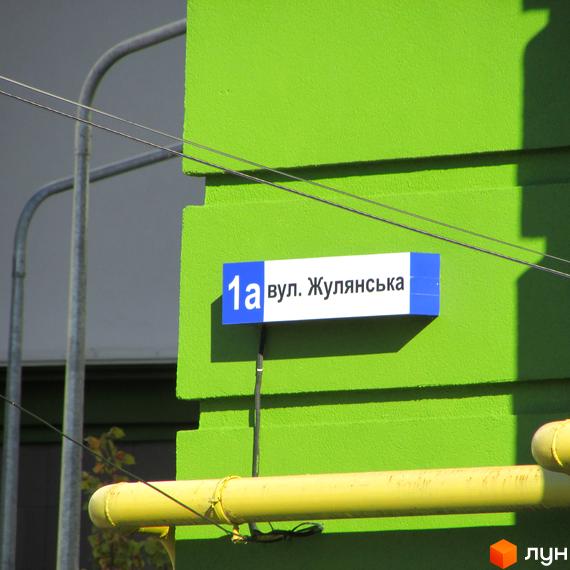 Фасад новобудови ЖК Евромісто з табличкою вулиці. Навколо будівлі видно елементи прибудинкової території, включаючи труби та кабелі.