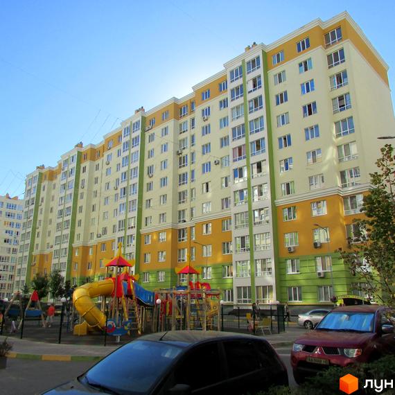 Житловий комплекс Евромісто з яскравою фасадною обробкою та дитячим майданчиком. Багатоповерховий будинок з великою кількістю вікон та балконів.