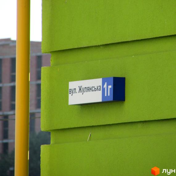На фасаді новобудови ЖК Евромісто табличка з адресою вул. Жулянська, 1г. Зелений колір стіни та жовта колона поруч.