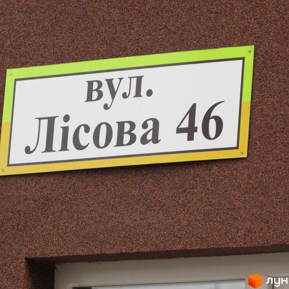 Вивіска з адресою вул. Лісова 46 на фоні стіни будинку. Затишна прибудинкова територія з зеленими насадженнями.