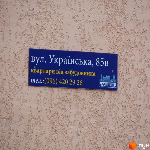 Назва житлового комплексу: вул. Українська, 85в. Квартири від забудовника. Телефон: (096) 420 29 26. На вивісці також присутній логотип компанії 