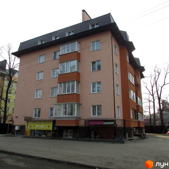 Зовнішній вигляд будинку на вул. Українська, 85в. Фасад будинку світло-персикового кольору з коричневими елементами. Біля будинку розташована прибудинкова територія з тротуаром та деревами.