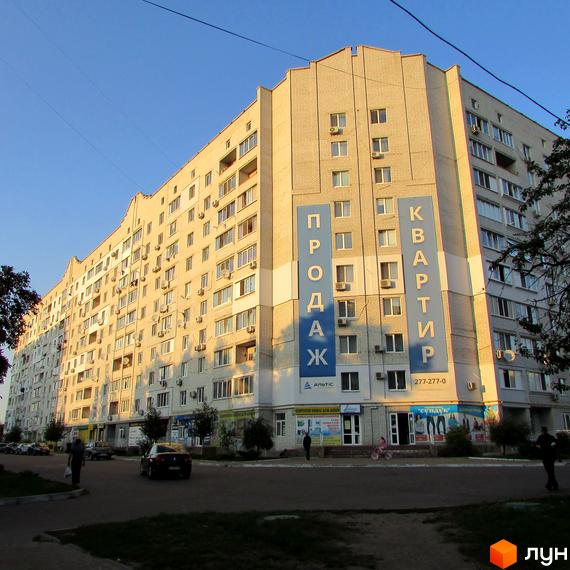 Багатоповерховий житловий будинок світлої цегли з оголошеннями про продаж квартир та магазинами на першому поверсі. Поруч вулиця.