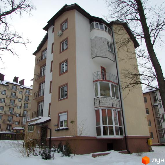 Житловий комплекс Джерело - багатоповерховий будинок з балконами та вікнами, розташований на фоні дерев та снігу. Навколо будинку видно прибудинкову територію з деревами та кущами.