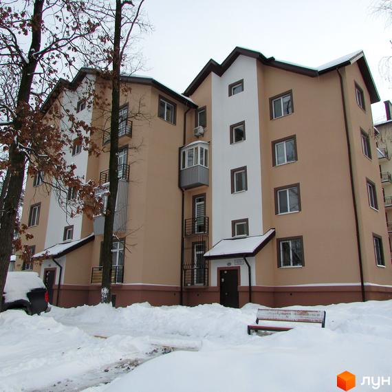 Зовнішній вигляд триповерхового будинку ЖК Джерело взимку, з білими та бежевими фасадами, балконами та вікнами. На прибудинковій території багато снігу, видно дерева та лавку.