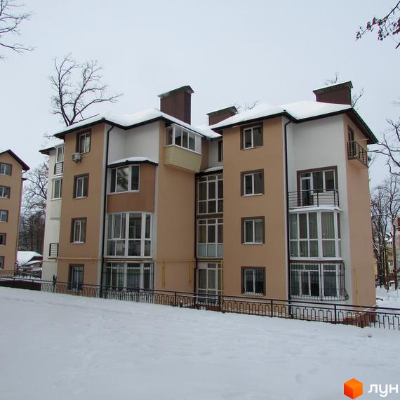 Зовнішній вигляд триповерхового будинку ЖК Джерело з коричневими дахами та світло-бежевими стінами, засніжена прибудинкова територія з огорожею.