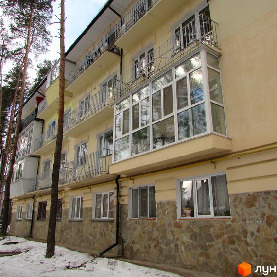 Житловий комплекс на вул. Рильського, 7, з балконами та великими вікнами. Прибудинкова територія з зеленими насадженнями та засніженим покриттям.