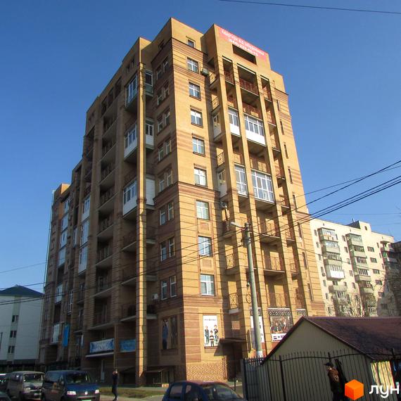 Багатоповерховий житловий будинок на вулиці Шевченка, 4, збудований з цегли світло-коричневого кольору, має багато вікон та балконів. На вулиці припарковані автомобілі.