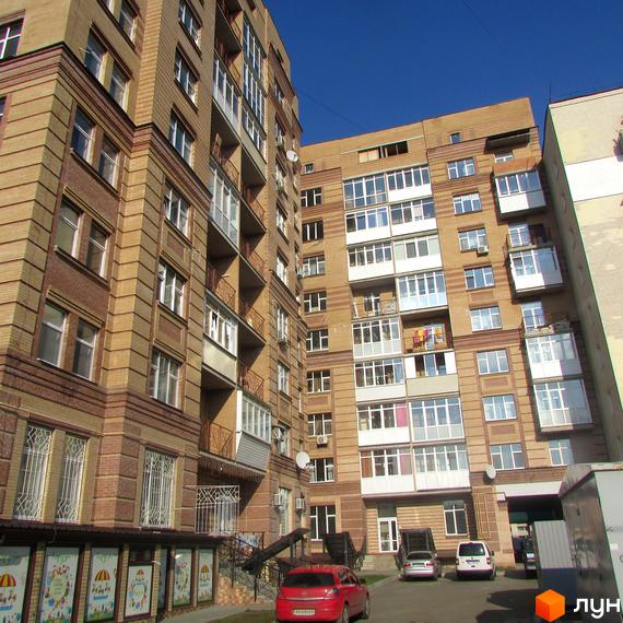 Житловий комплекс на вул. Шевченка, 4 з цегляною фасадною обробкою та балконами. Прибудинкова територія з автомобілями та зеленими насадженнями.