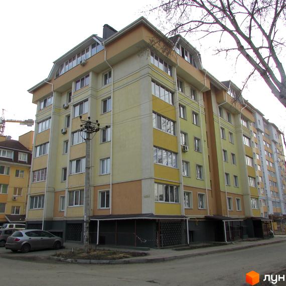 Житловий комплекс на вул. Мінеральна, 37 з жовто-помаранчевим фасадом та мансардним поверхом. Перед будинком видно дорогу, стовп та припарковані автомобілі.