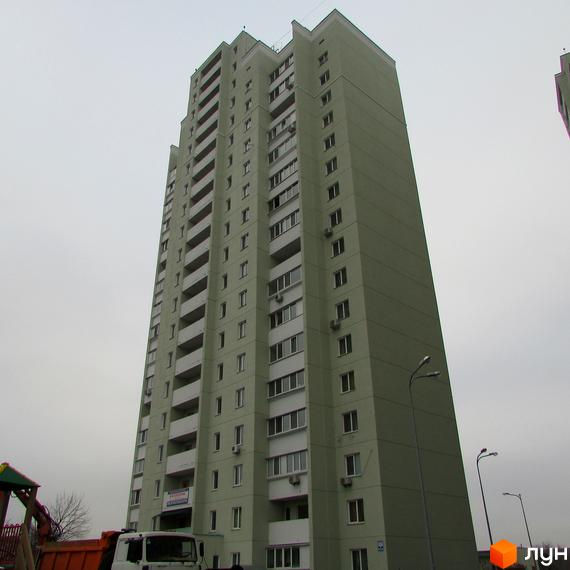 Високоповерхова новобудова світло-зеленого кольору з численними балконами та вікнами. На прибудинковій території видно частину дитячого майданчика та вантажівку.