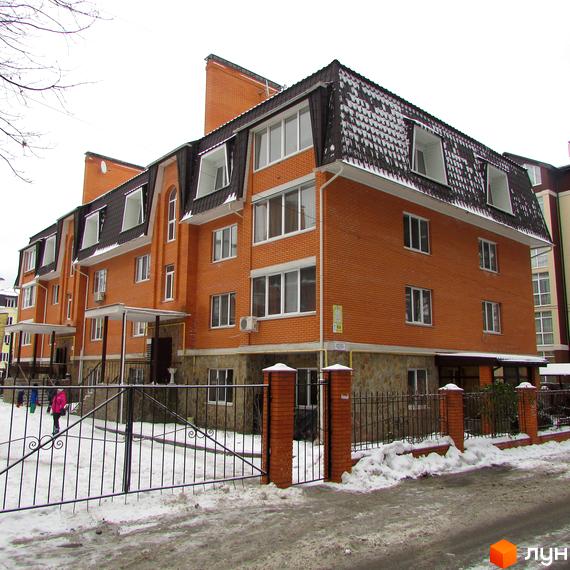 Житловий комплекс на вул. Лермонтова, 6, з червоної цегли та дахом з черепиці, огороджений парканом. Прибудинкова територія засніжена.