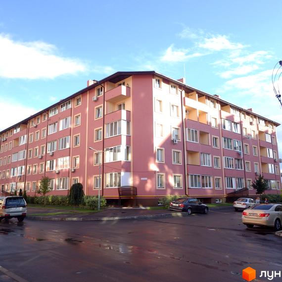 Житловий комплекс Щасливий у рожевих тонах з великою кількістю вікон. Прибудинкова територія з припаркованими автомобілями та зеленими насадженнями.