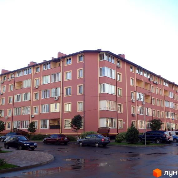 Житловий комплекс Щасливий - це багатоповерховий будинок з червоною цегляною фасадною частиною та жовтими декоративними елементами. Навколо будинку розташовані дерева та припарковані автомобілі.