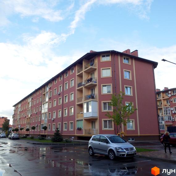 Житловий комплекс Щасливий – багатоповерховий будинок з балконами та вікнами, прибудинкова територія з автомобілями та мокрим асфальтом.