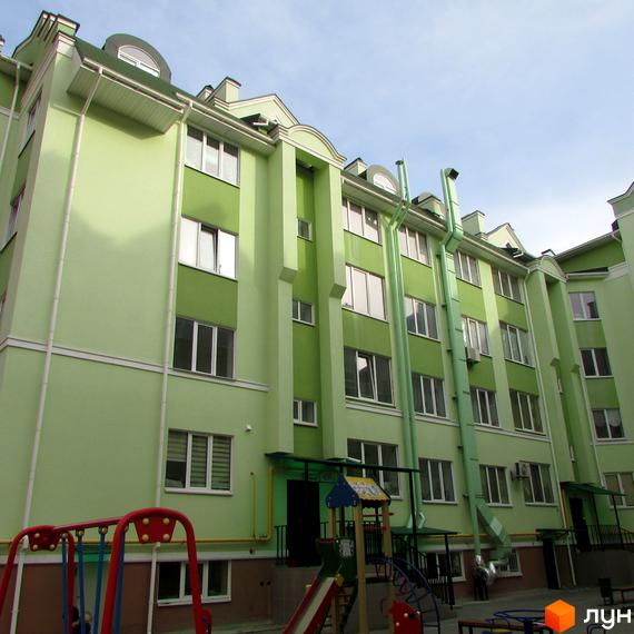 Зовнішній вигляд світло-зеленої новобудови ЖК Академквартал з вікнами та балконами. На прибудинковій території дитячий майданчик з гіркою та гойдалкою.