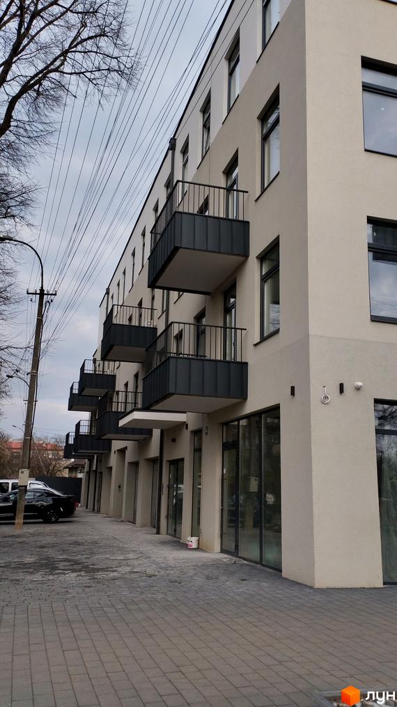 Зовнішній вигляд будинку на вулиці Закарпатська, 22. Фасад будівлі з балконами та великими вікнами, а також тротуарна доріжка.