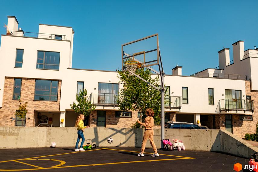 Котеджне містечко КМ Липові Роси. Діти грають у баскетбол на подвір'ї біля сучасних будинків з цегляними та білими фасадами.