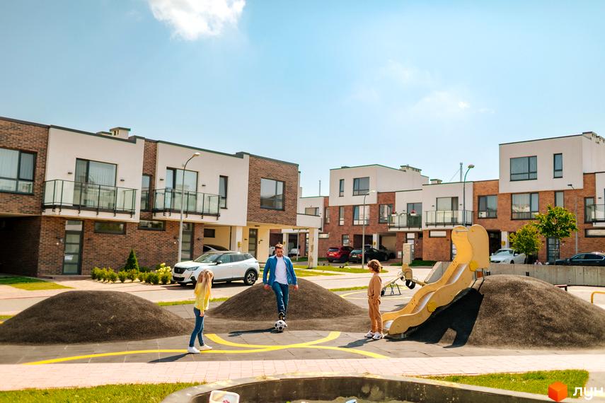 Котеджне містечко КМ Липові Роси: сучасні триповерхові будинки з цегляним фасадом та білими елементами. На прибудинковій території дитячий майданчик з гіркою та зелені насадження.