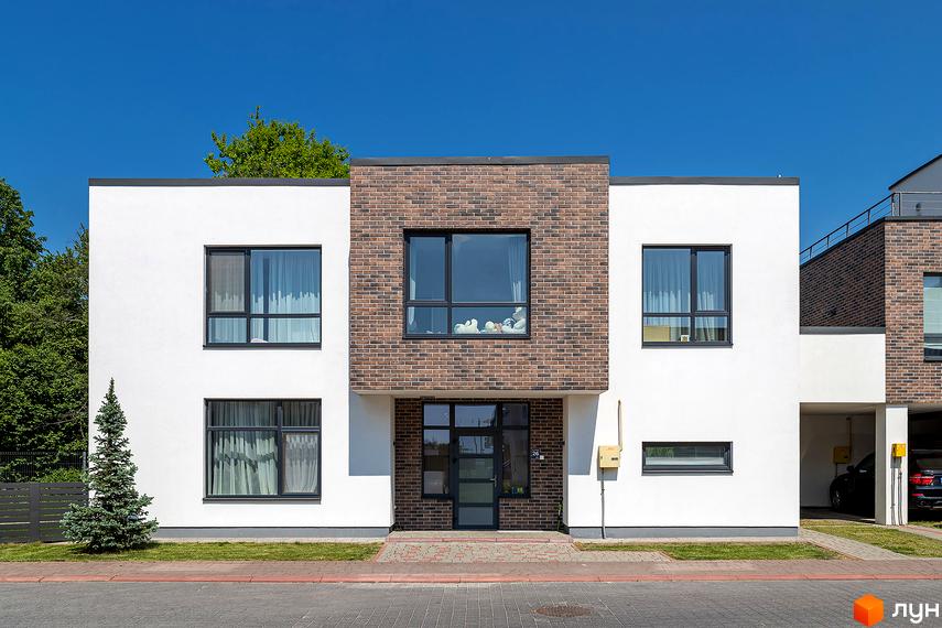 Котеджне містечко КМ Липові Роси: двоповерховий будинок з білою та цегляною обробкою, великими вікнами та входом. Прибудинкова територія з деревами та бруківкою.