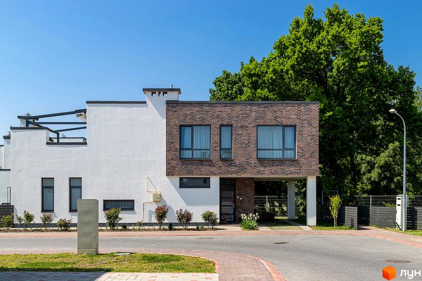 Котеджне містечко КМ Липові Роси. Фасад будинку з білої штукатурки та цегляної кладки, вікна з сірими рамами, зелені насадження та доглянута прибудинкова територія.