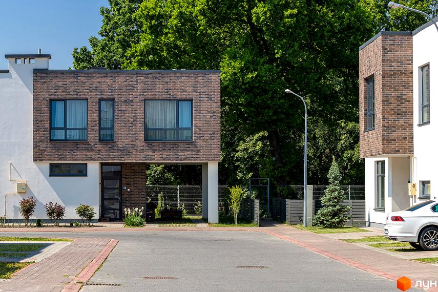 Котеджне містечко КМ Липові Роси. Фасад будинку оздоблений цеглою та білою штукатуркою. Біля будинку розташована зелена зона та паркан.