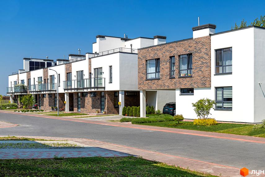 Котеджне містечко КМ Липові Роси: сучасні будинки з цегляними фасадами та скляними балконами. Зелена прибудинкова територія з доглянутими газонами та деревами.