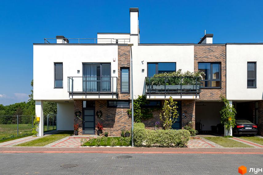 Котеджне містечко Липові Роси: фасади будинків з цегляним оздобленням та білою штукатуркою, балкони зі скляними огорожами, зелені насадження та доглянута прибудинкова територія.