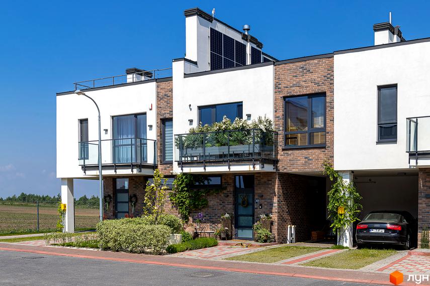 Котеджне містечко КМ Липові Роси: фасади будинків з цегляним оздобленням, балконами та сонячними панелями. Прибудинкова територія з доглянутим ландшафтом та автомобілем.