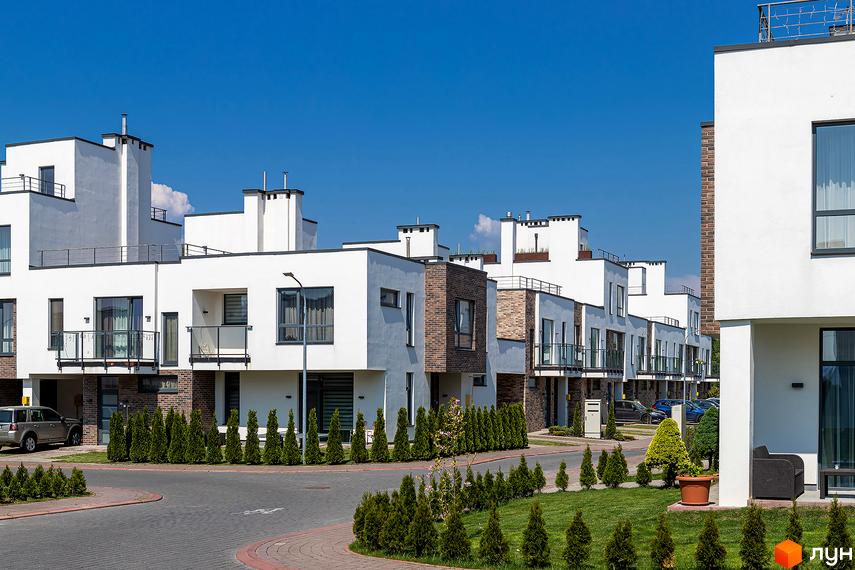 Котеджне містечко КМ Липові Роси: білі двоповерхові будинки з цегляними вставками та балконами. Озеленена прибудинкова територія з доглянутими газонами та туями.