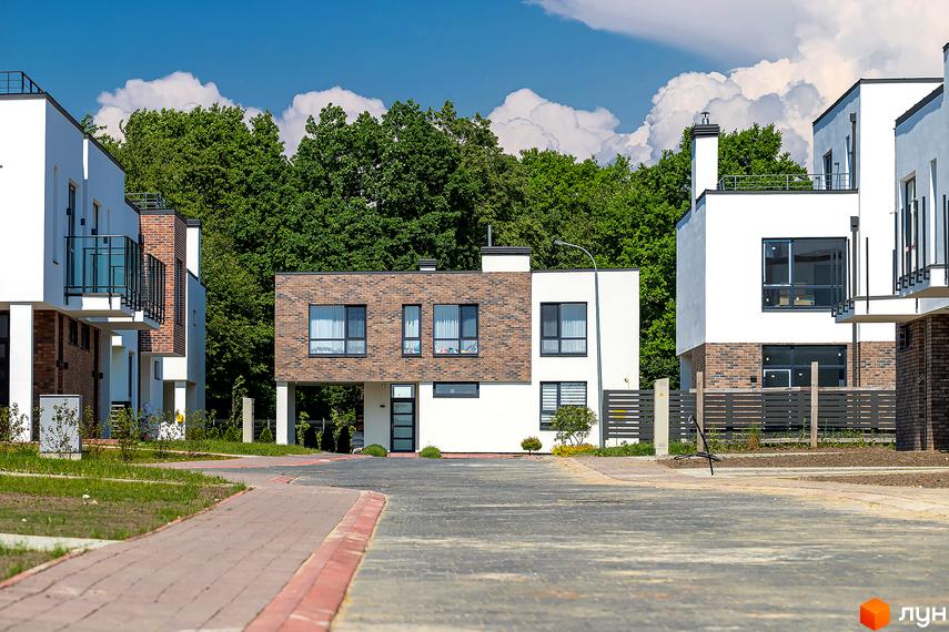 Котеджне містечко Липові Роси: фасади будинків з цегляним оздобленням та білою штукатуркою, зелені насадження та доглянута прибудинкова територія.